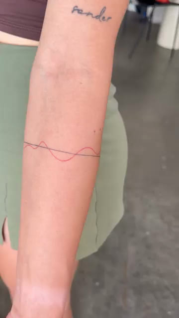 Thin armband of one black line and one red wave, healed fine line tattoo