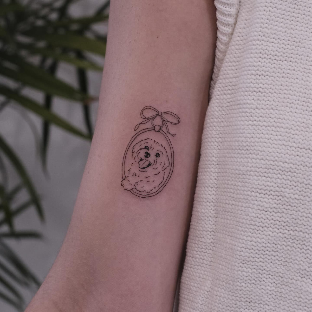 Small fluffy dog in an oval frame with a bow, fine line tattoo