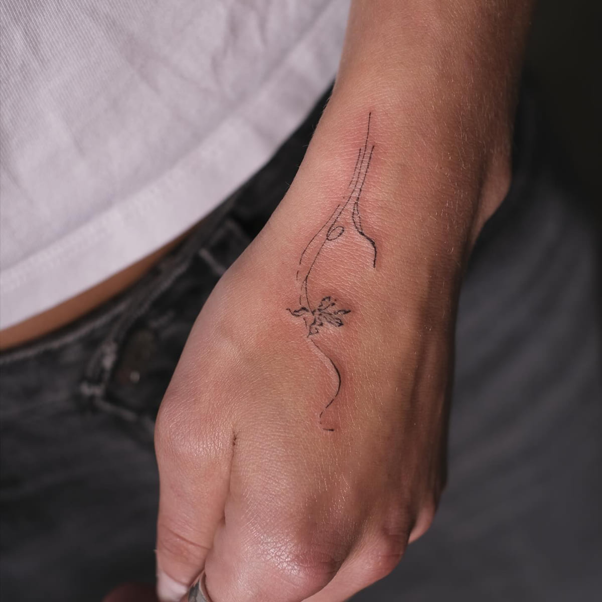 Fine stem with a small flower running from wrist onto the hand, fine line tattoo