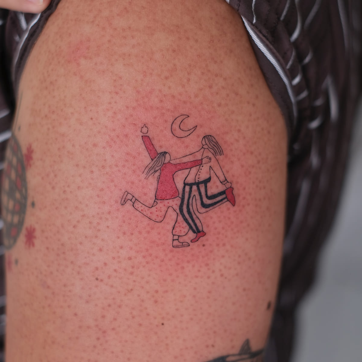 Two friends dancing under a moon, one in red, fine line tattoo