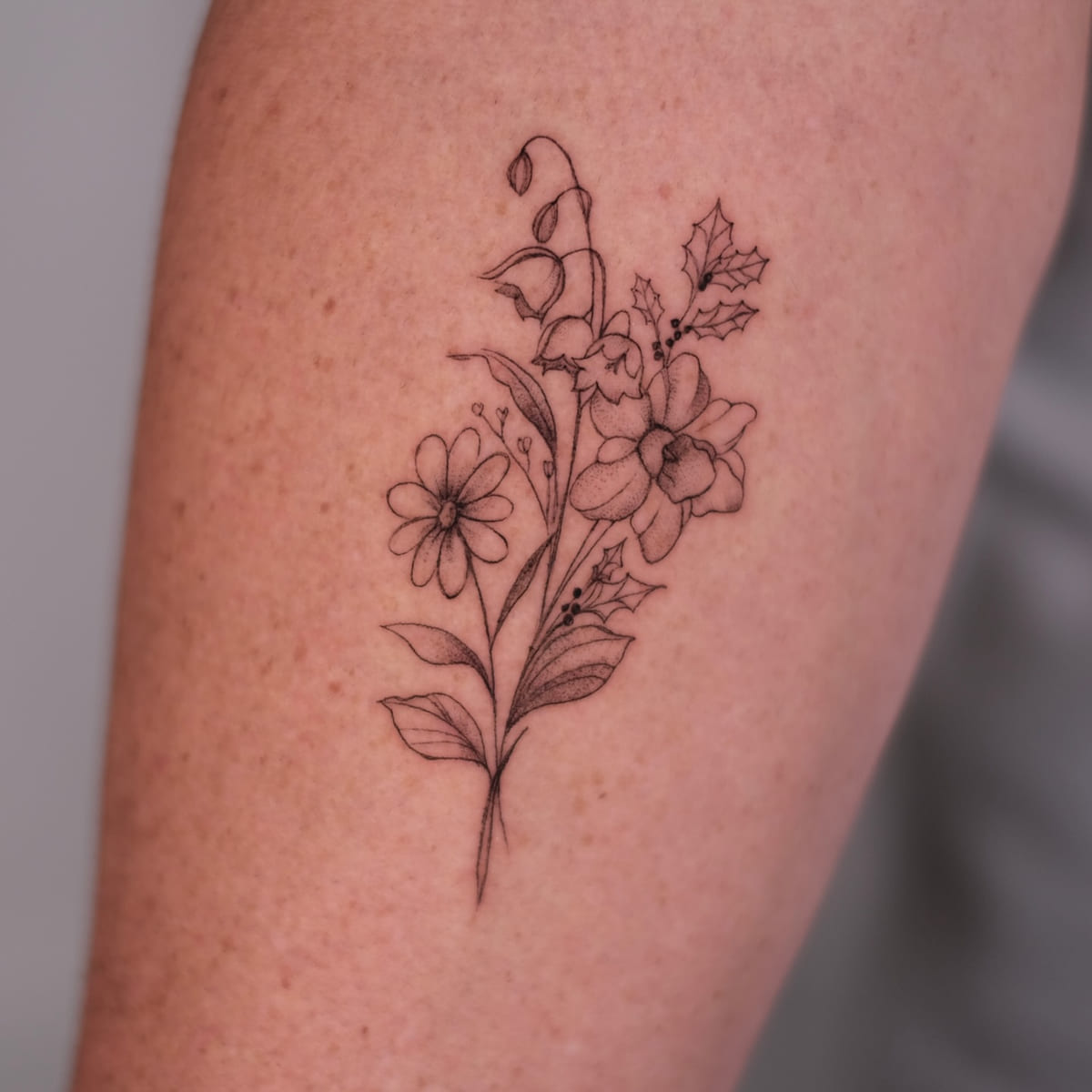 Bouquet of daisy, lily of the valley, holly and narcissus, fine line tattoo