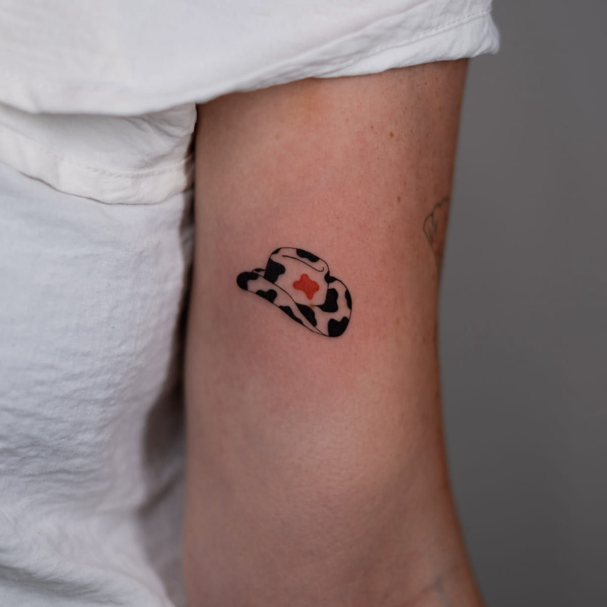 Cow print cowboy hat with a red heart, fine line tattoo