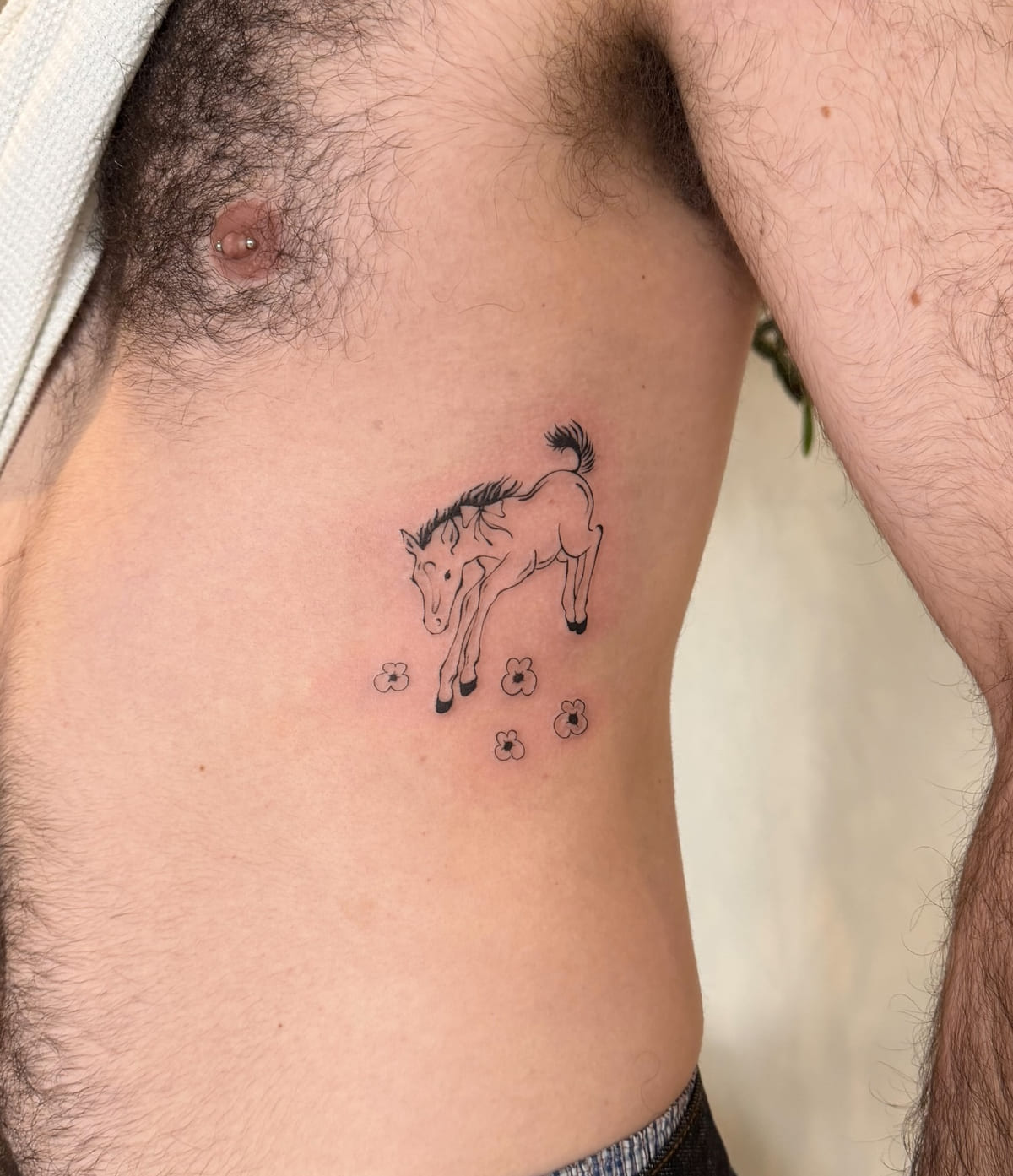 Leaping foal over small flowers, fine line tattoo