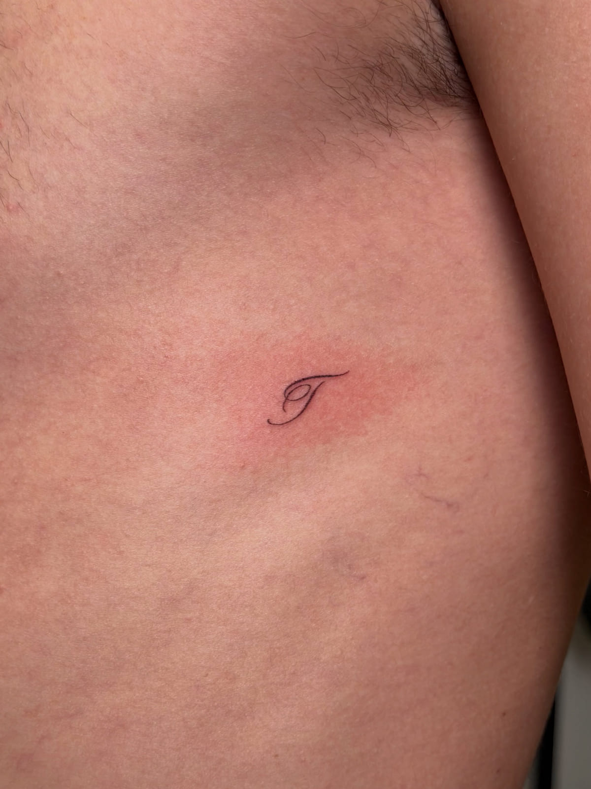 Tiny script initial T, fine line tattoo