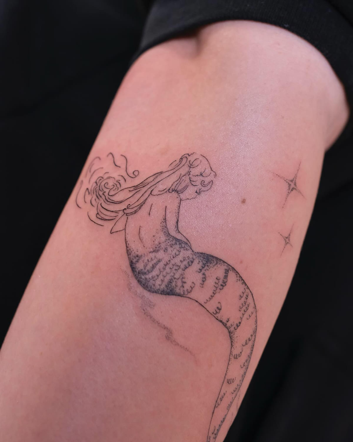 Mermaid seen from behind with wind swept hair and sparkles, fine line tattoo