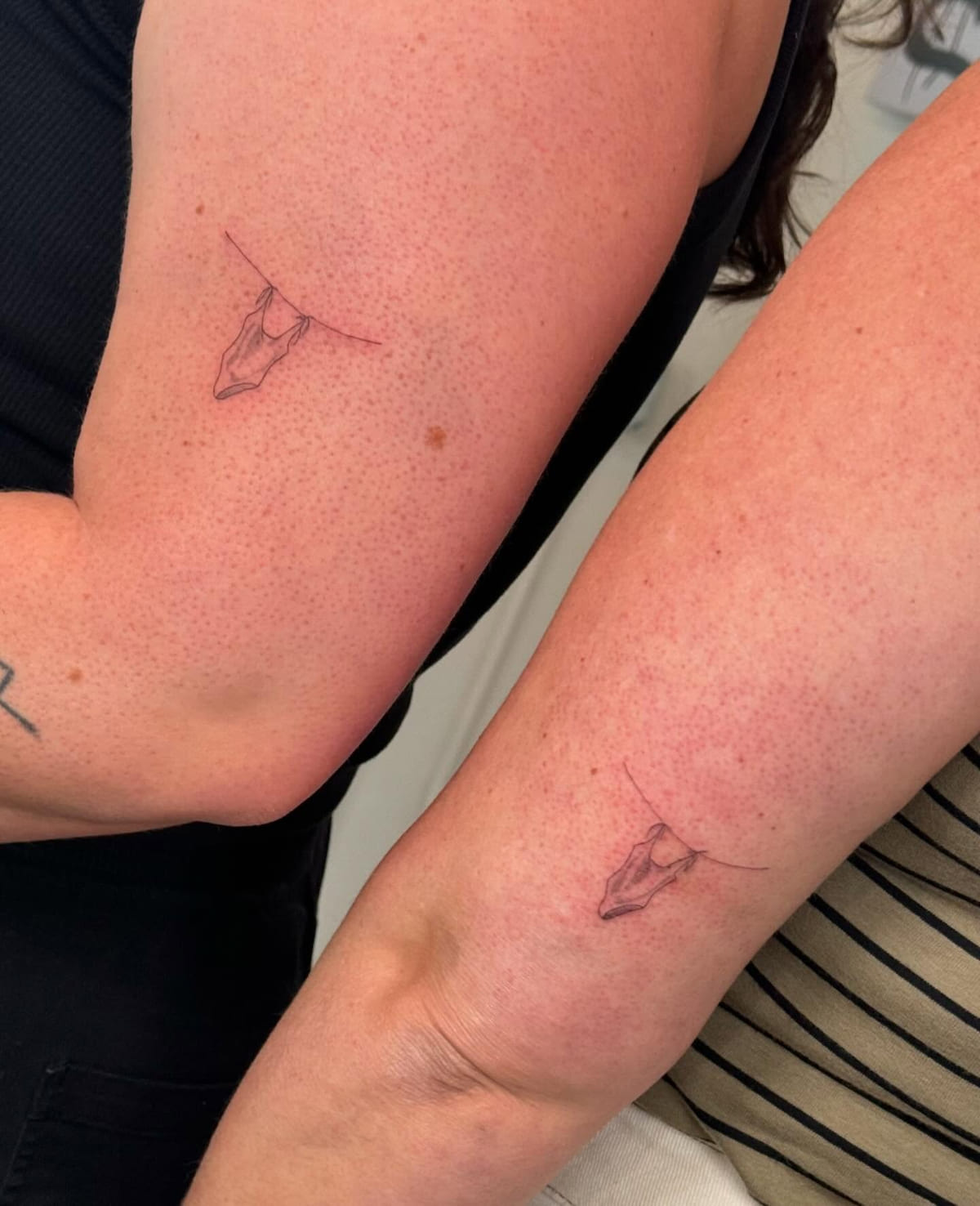 Two people with matching small gems hanging on a thread, fine line tattoo
