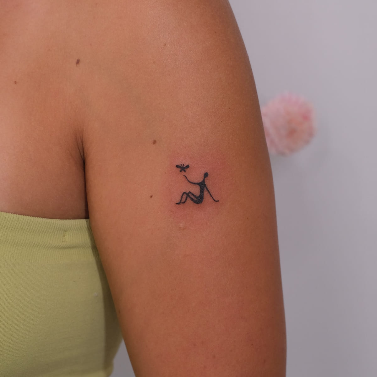 Tiny seated figure with a bird, solid black, fine line tattoo