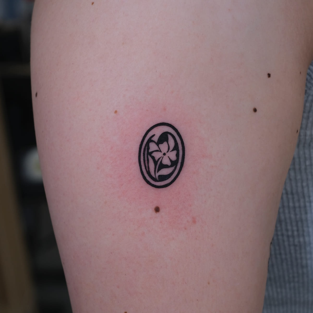 Flower inside a solid black oval, fine line tattoo