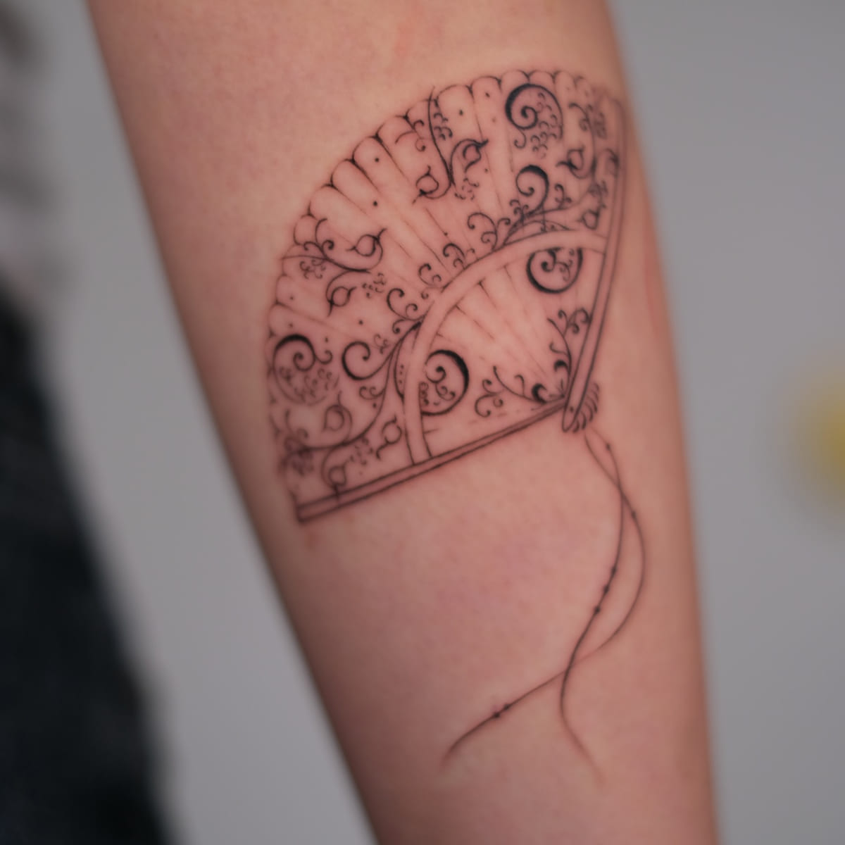 Ornate lace hand fan with a tassel, fine line tattoo