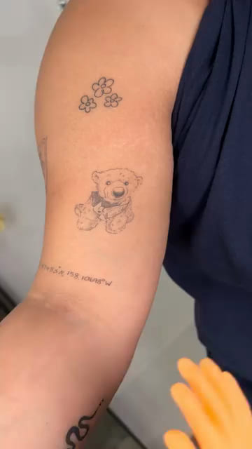 Small teddy bear on a forearm, closer, healed fine line tattoo