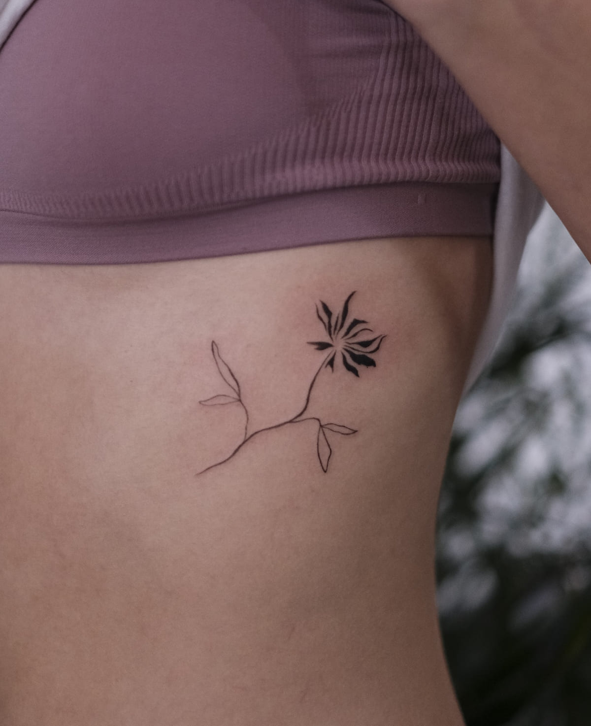 Sprig with a single solid black flower, fine line tattoo