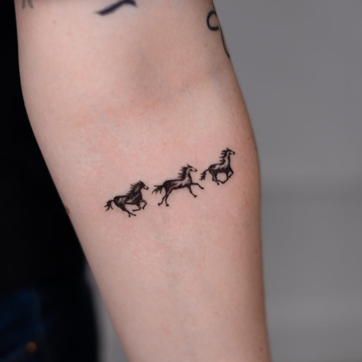 Three running horses in solid black, fine line tattoo