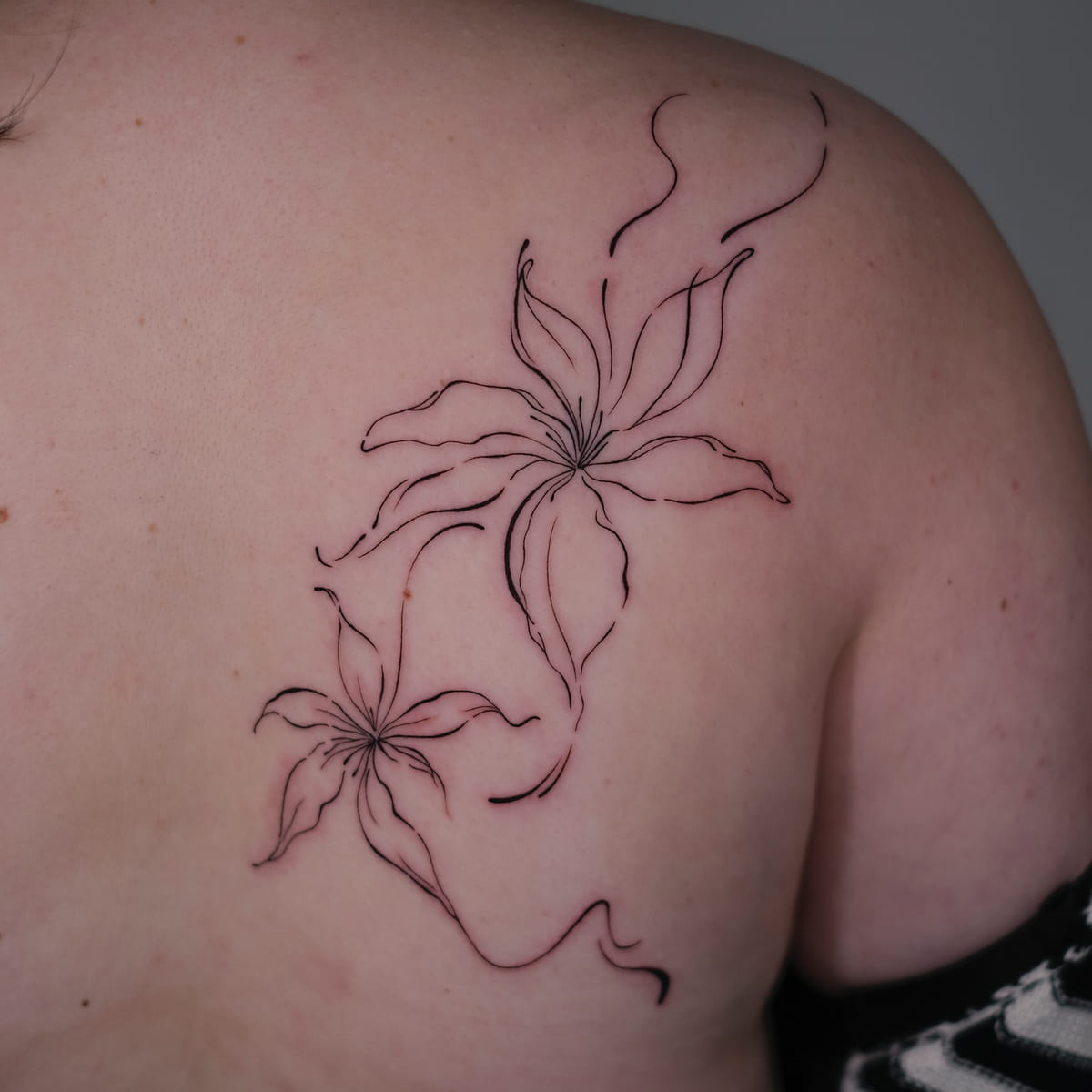 Two large lilies in flowing line across the shoulder blade, another view