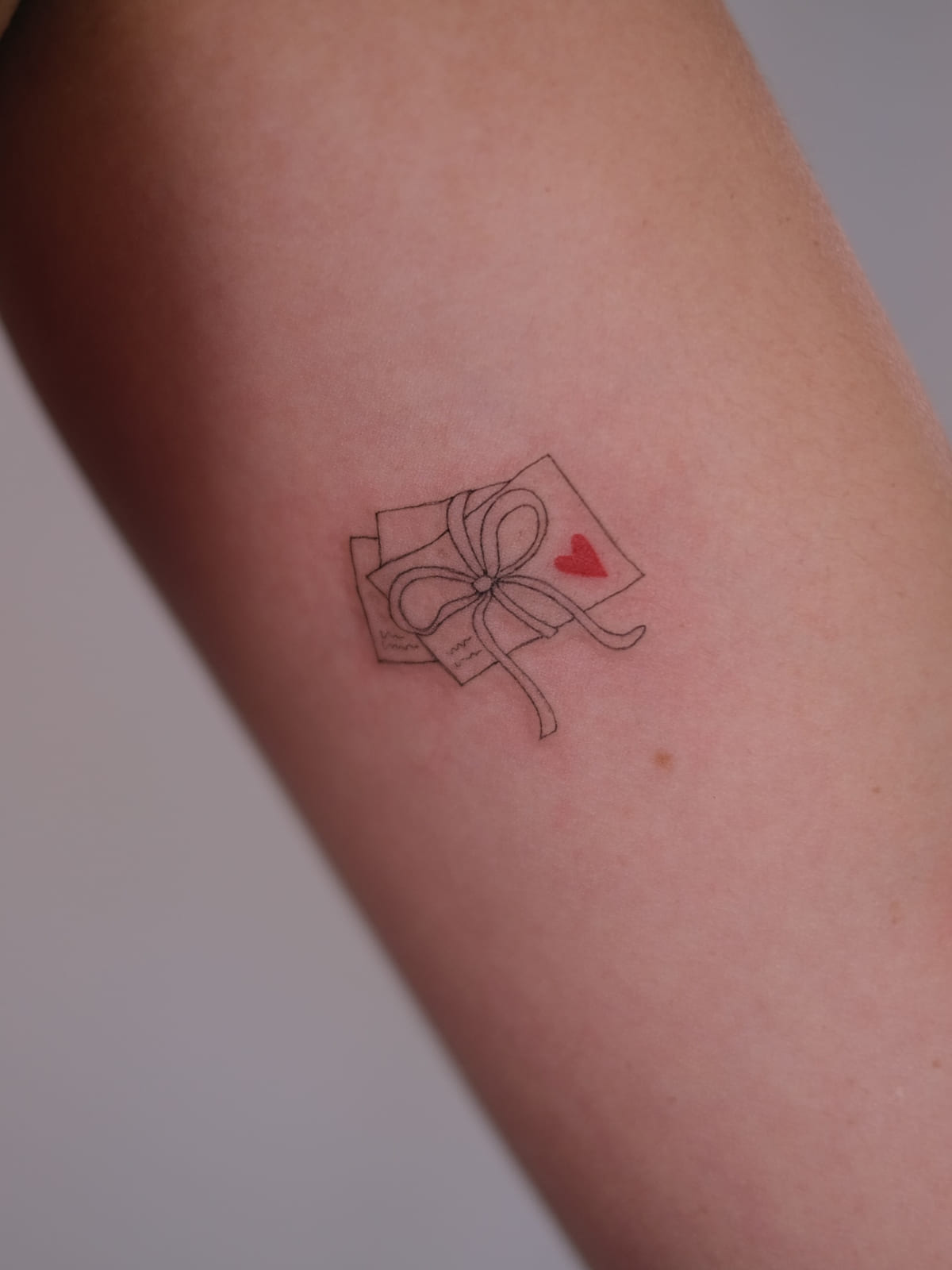 Stack of letters tied with a bow, one red heart, fine line tattoo