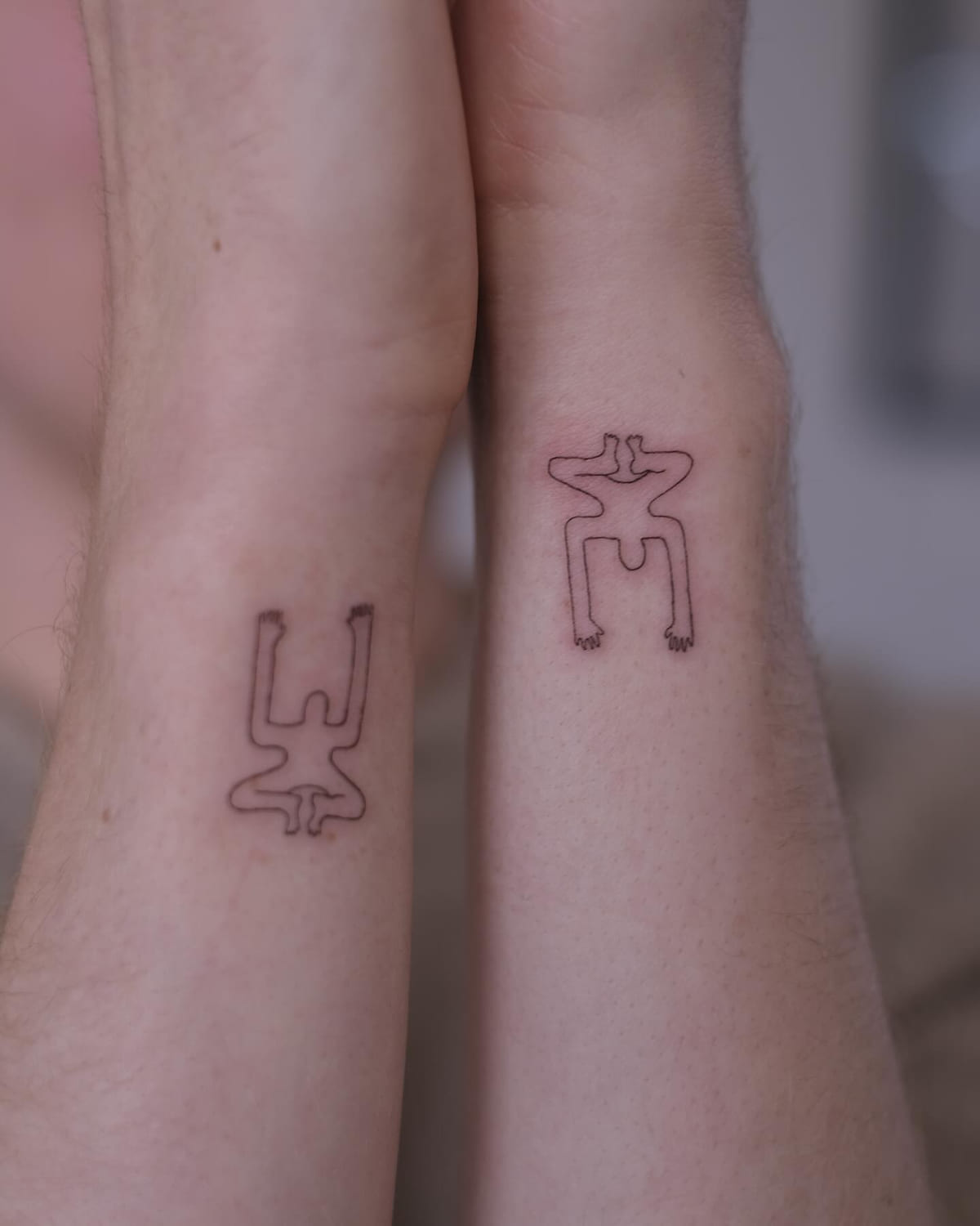 Two small single line figures, one on each wrist, fine line tattoo