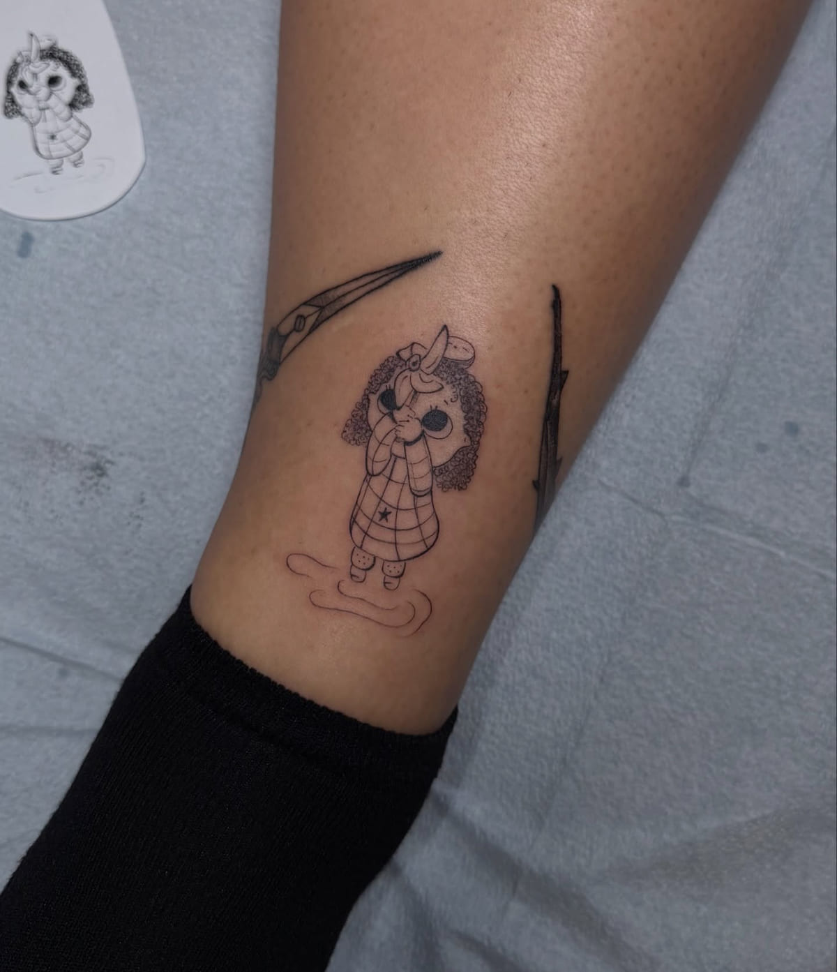 Doll like girl in a checked coat standing in a puddle, fine line tattoo