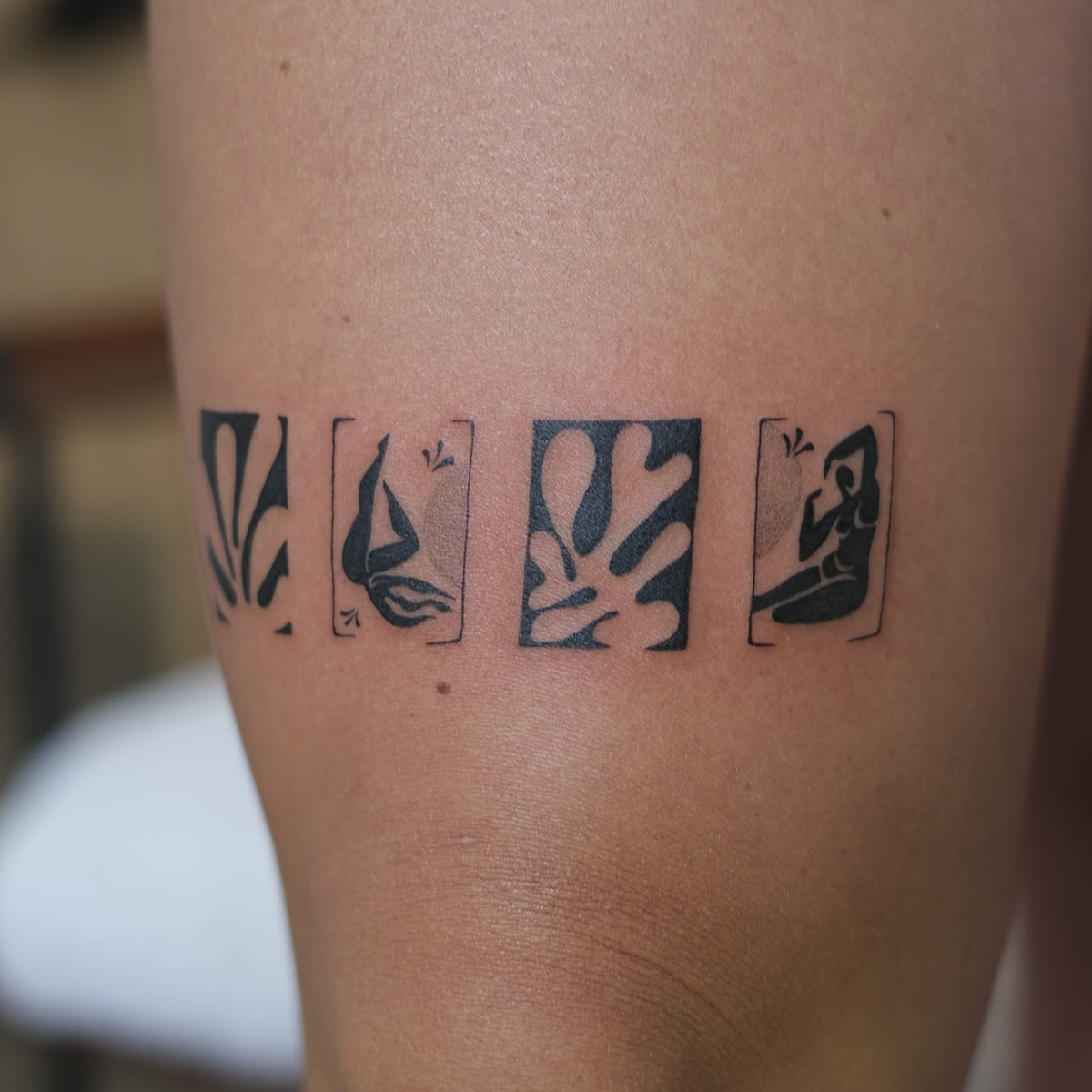 Band of four Matisse cut outs above the knee: leaf forms and blue nudes in solid black, fine line tattoo