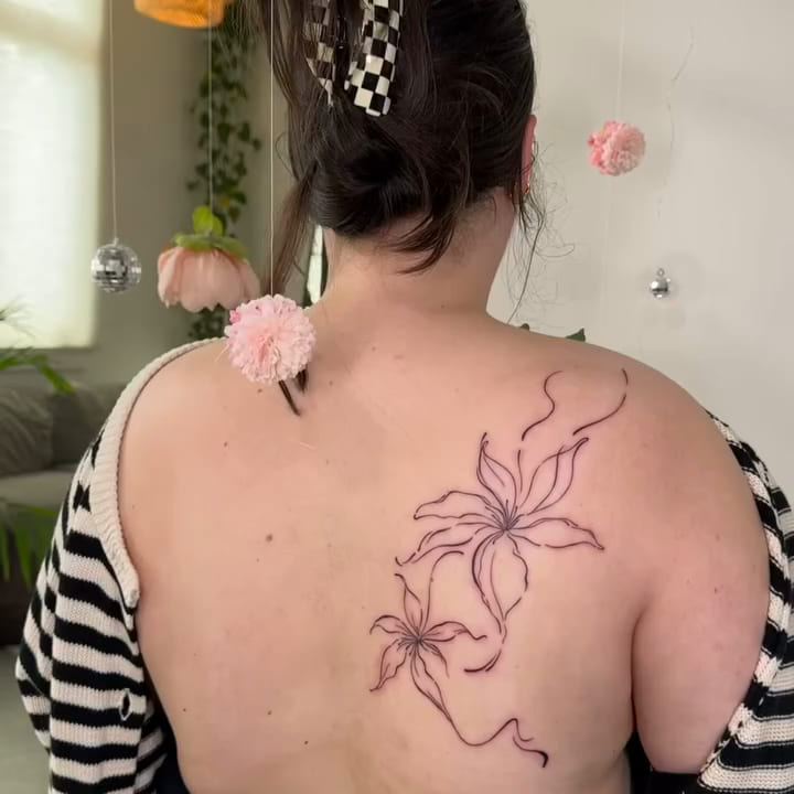 Two large lilies in flowing line across the shoulder blade, fine line tattoo