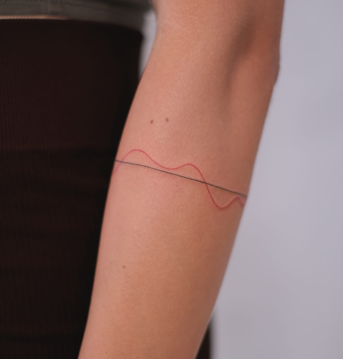 Thin armband of one black line and one red wave, healed fine line tattoo, the day it was made