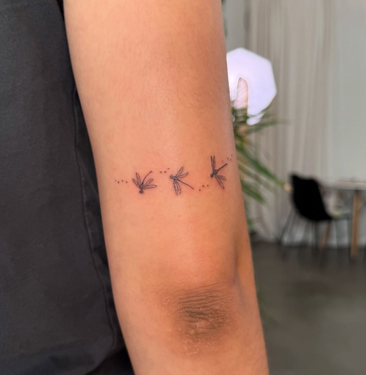 Three tiny dragonflies with dotted trails, fine line tattoo