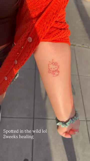 Red Hello Kitty on a forearm, healed fine line tattoo