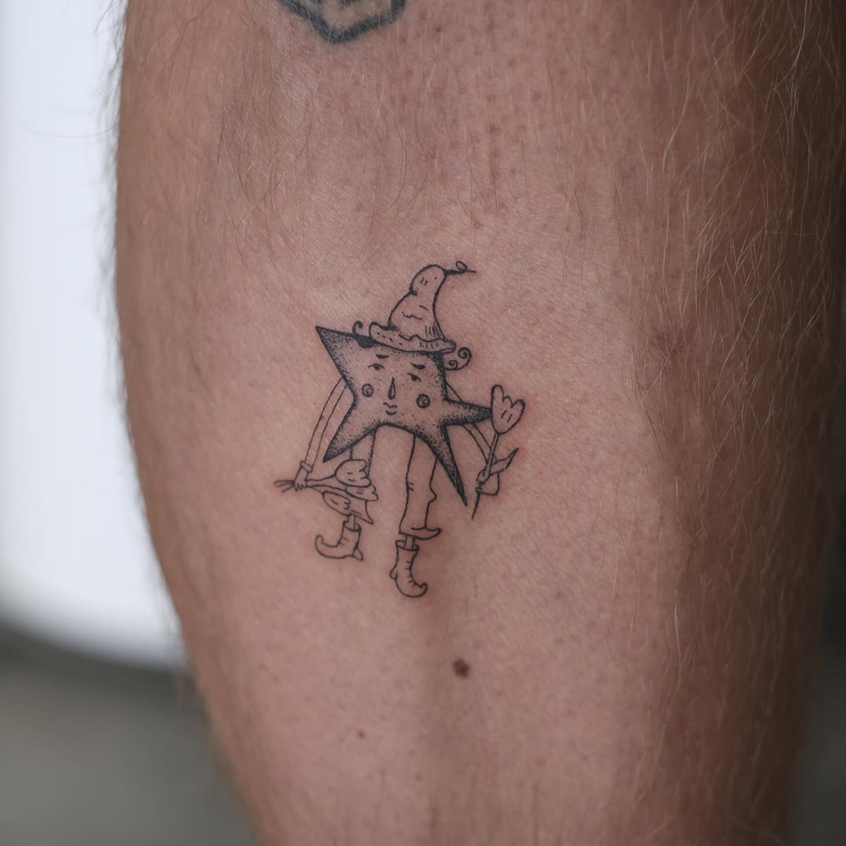 Star character in a wizard hat and boots holding a flower, fine line tattoo