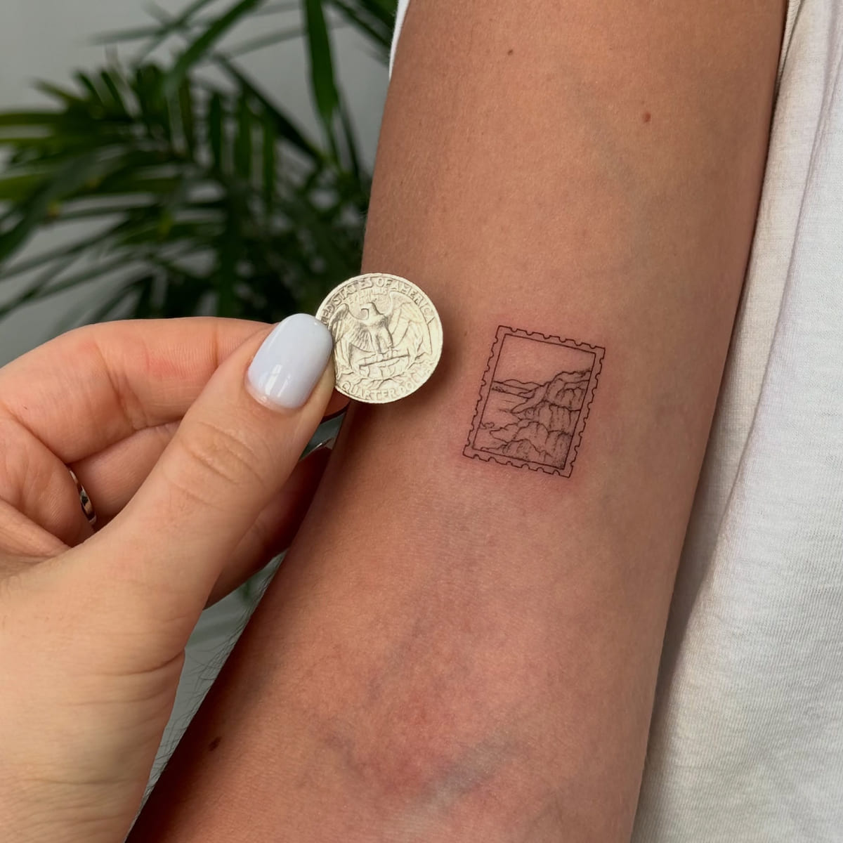 Postage stamp with a mountain, shown beside a quarter for scale, fine line tattoo