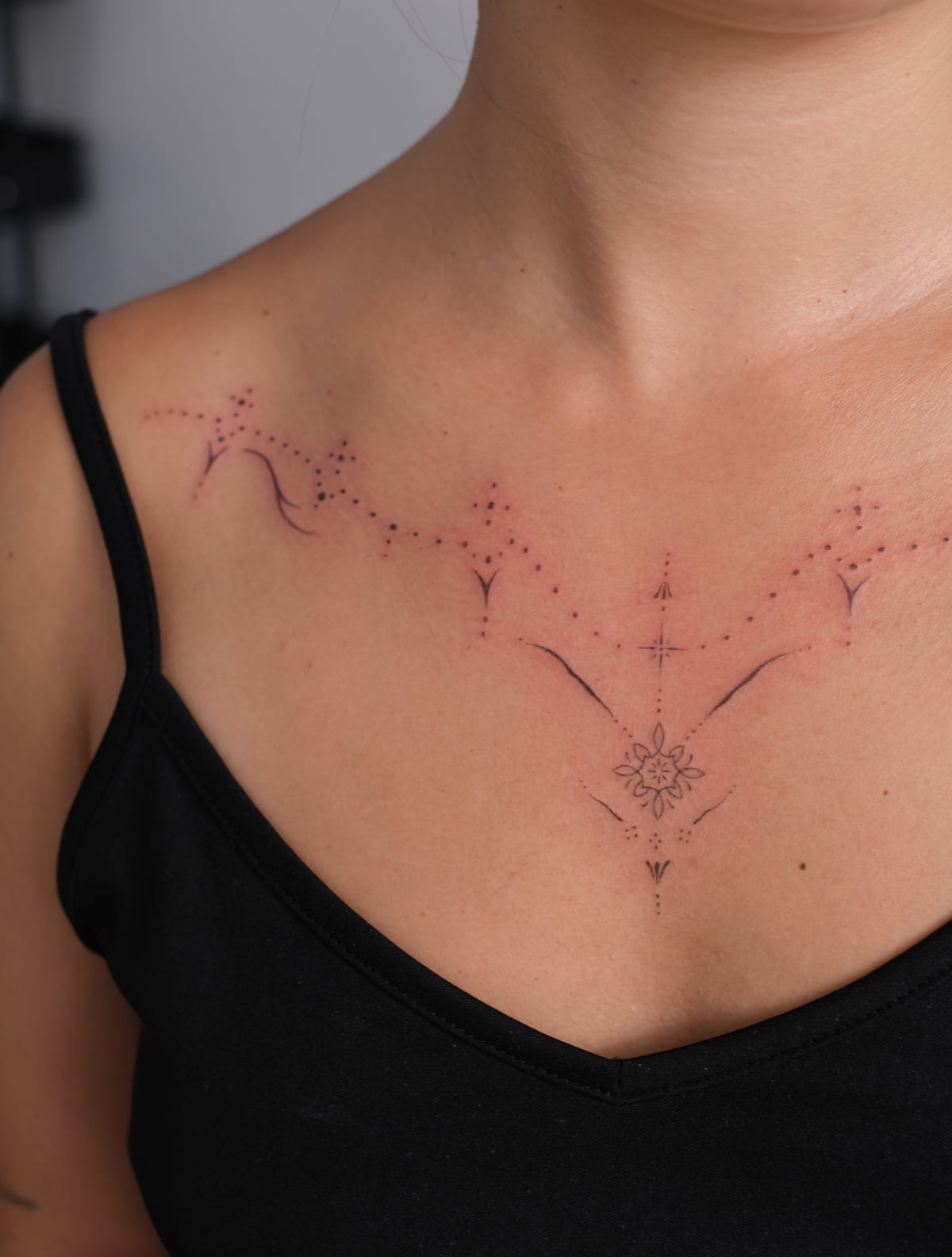 Dotwork necklace ornament across chest, fine line tattoo