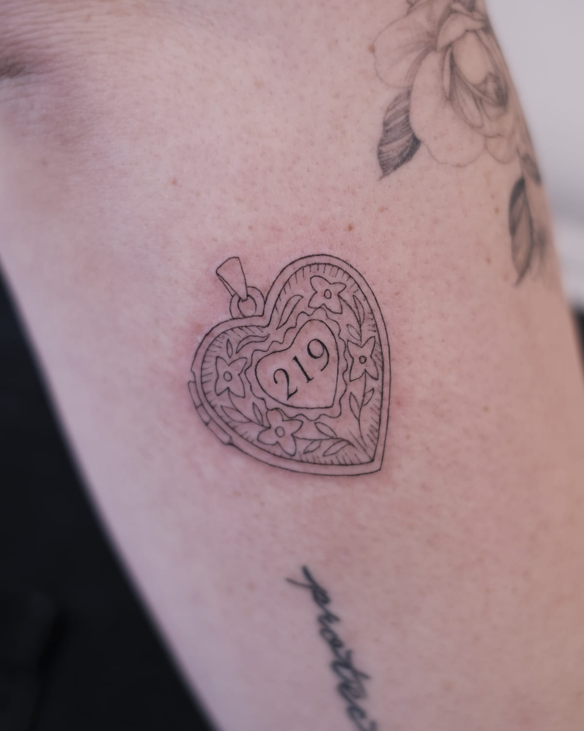 Engraved heart locket with the number 219, fine line tattoo