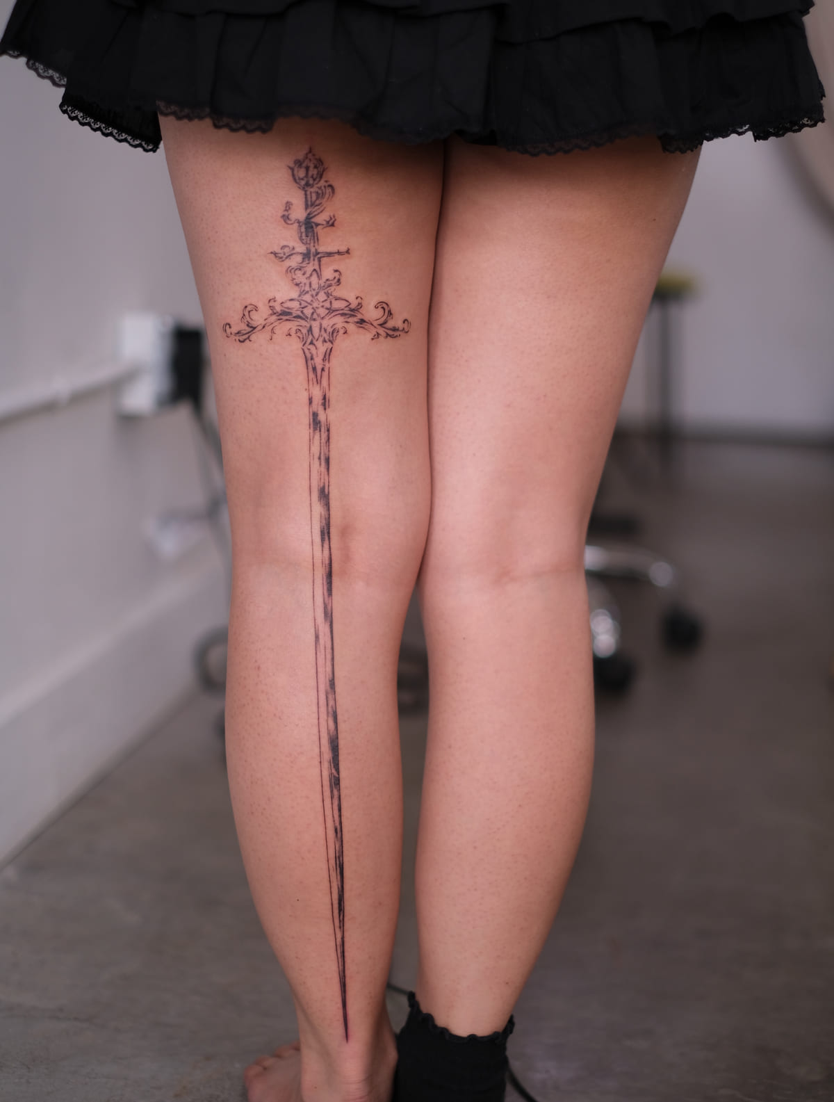 Long ornamental sword down the back of the leg, fine line tattoo