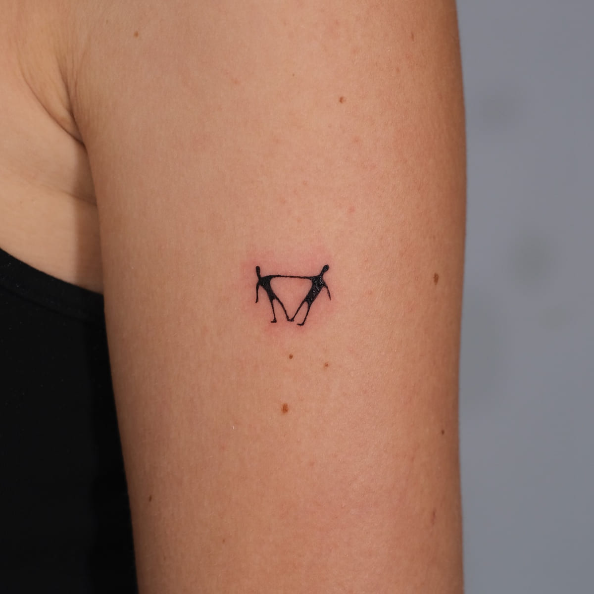 Two tiny dancing figures holding hands, solid black, fine line tattoo