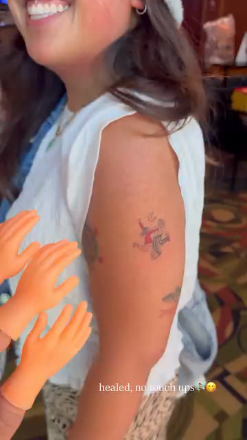 Small red and black piece on the back of an upper arm, healed fine line tattoo