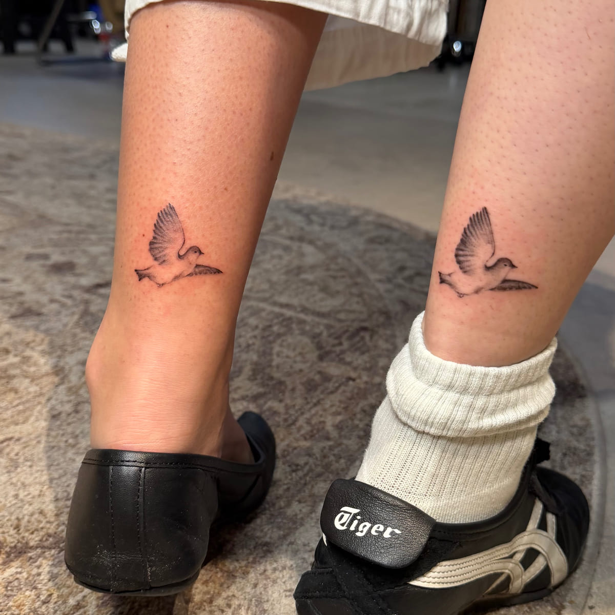 Matching doves in flight above the ankle on two people, fine line tattoo