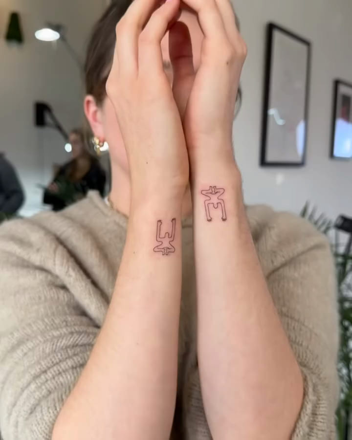 Two small single line figures, one on each wrist, fine line tattoo