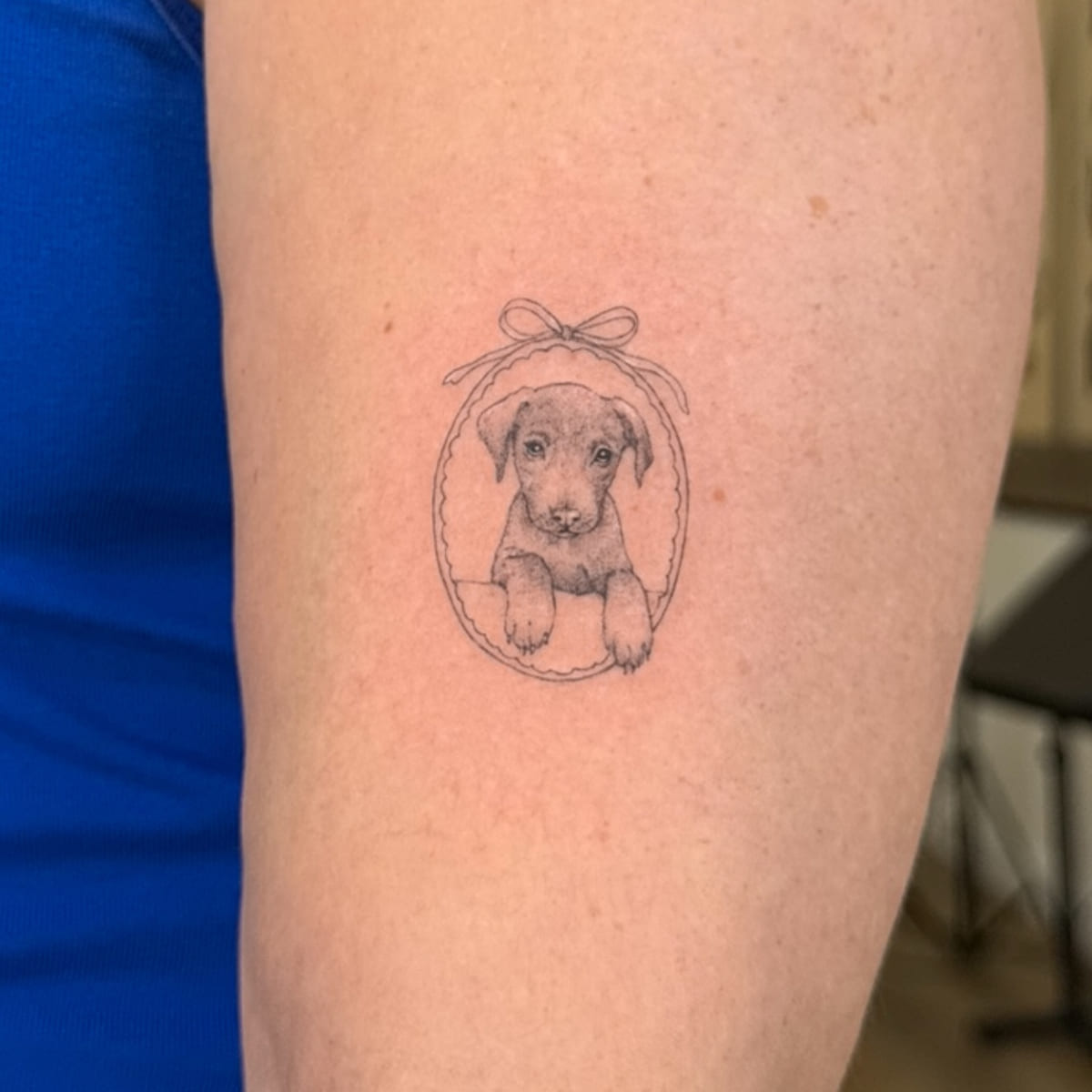 Puppy portrait in an oval frame with a bow, fine line tattoo