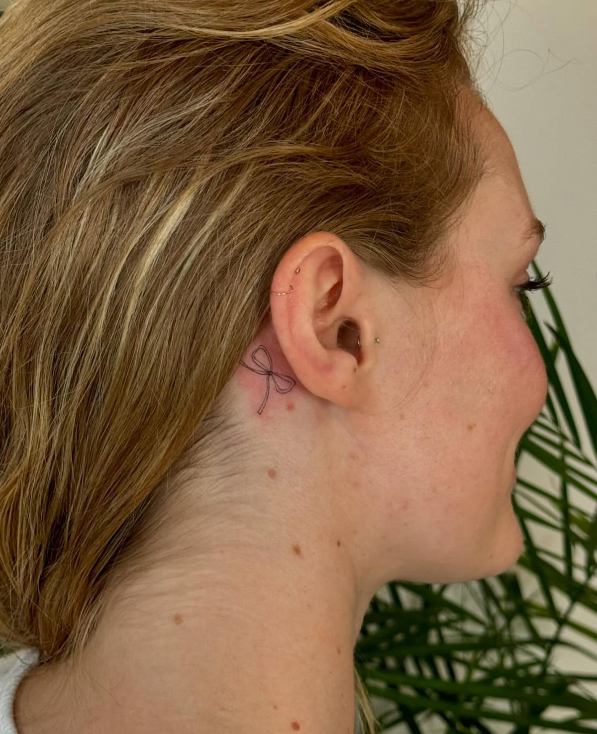Tiny bow behind the ear, fine line tattoo