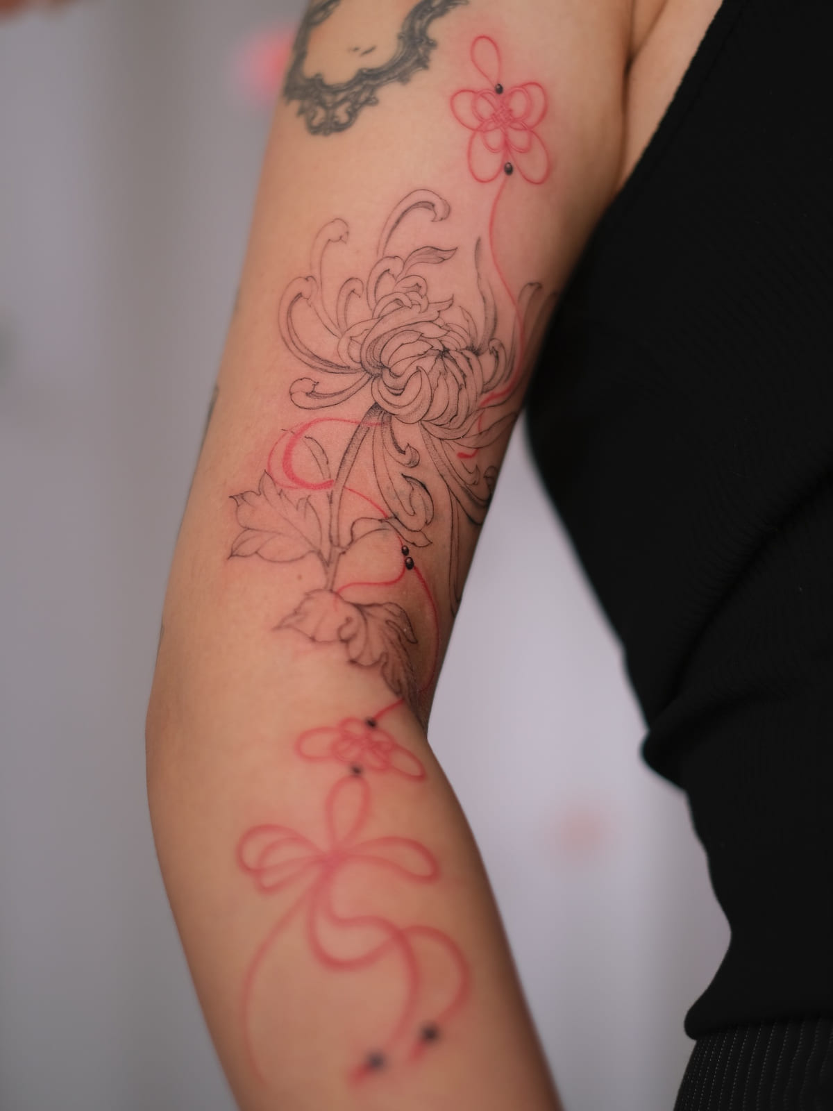 Chrysanthemum and flowers tied with red bows, running down the arm, fine line tattoo