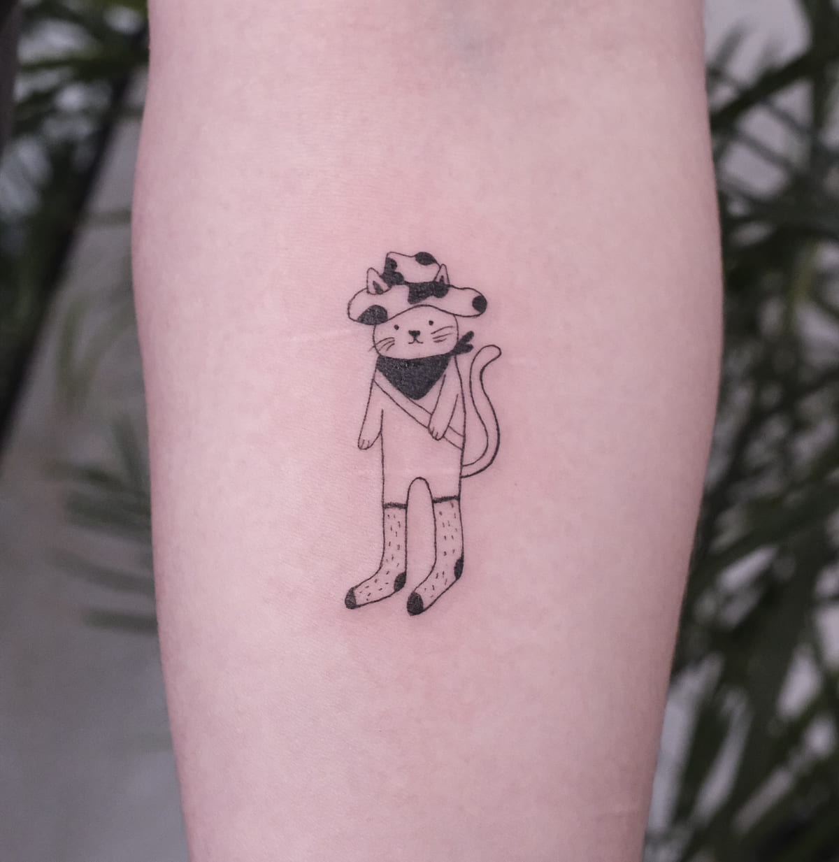 Cat in a cow print cowboy hat, bandana and socks, fine line tattoo
