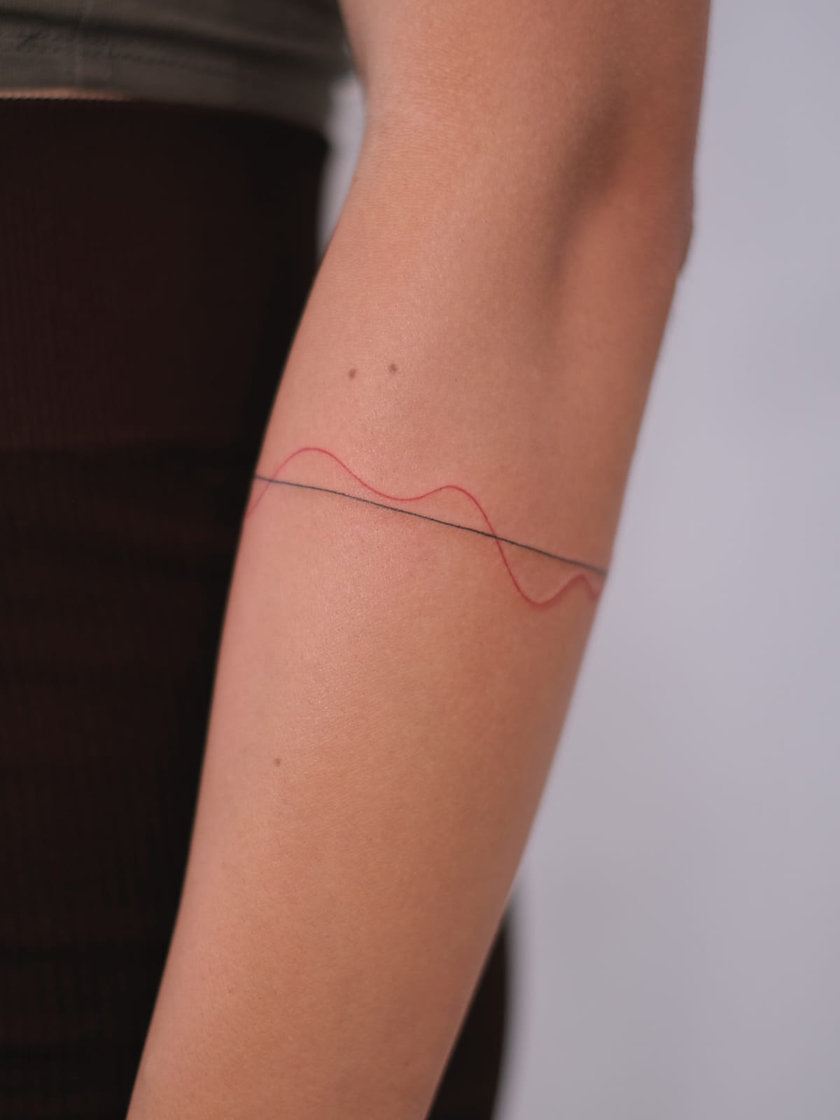 Thin armband of one black line and one red wave, fine line tattoo