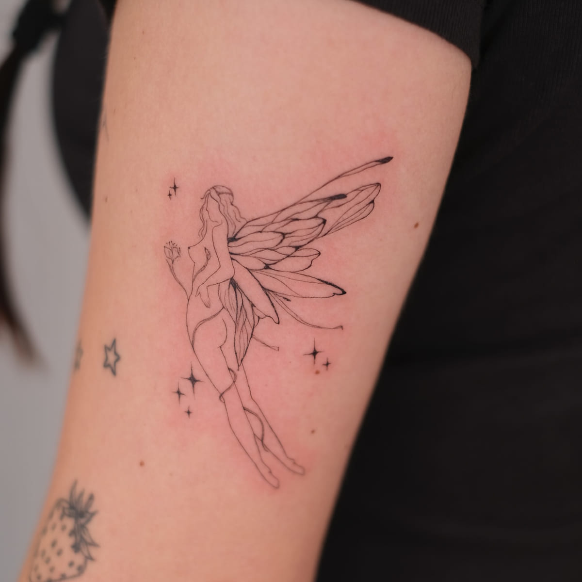 Fairy with long wings among sparkles, fine line tattoo