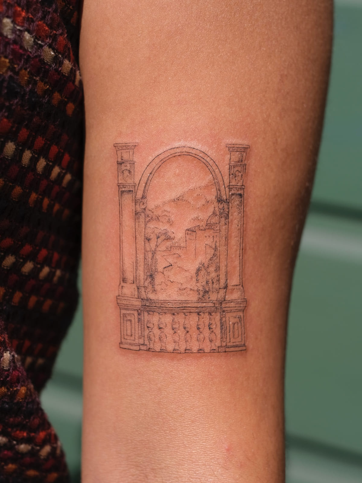 Arched window with columns and balustrade framing a hillside town, fine line tattoo