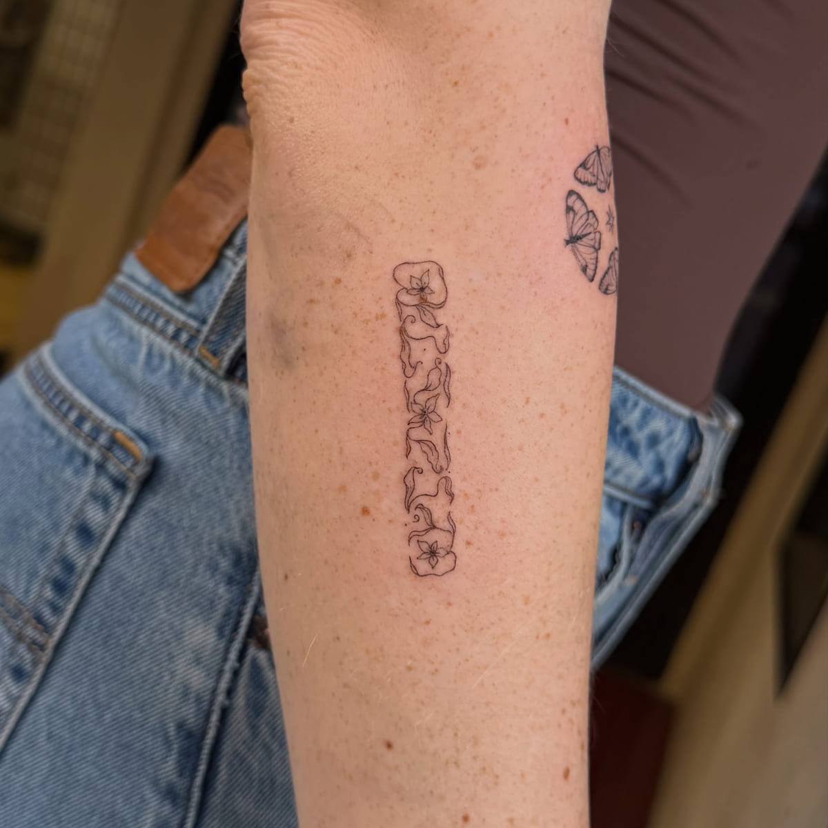 Vertical word in floral decorated letters, fine line tattoo