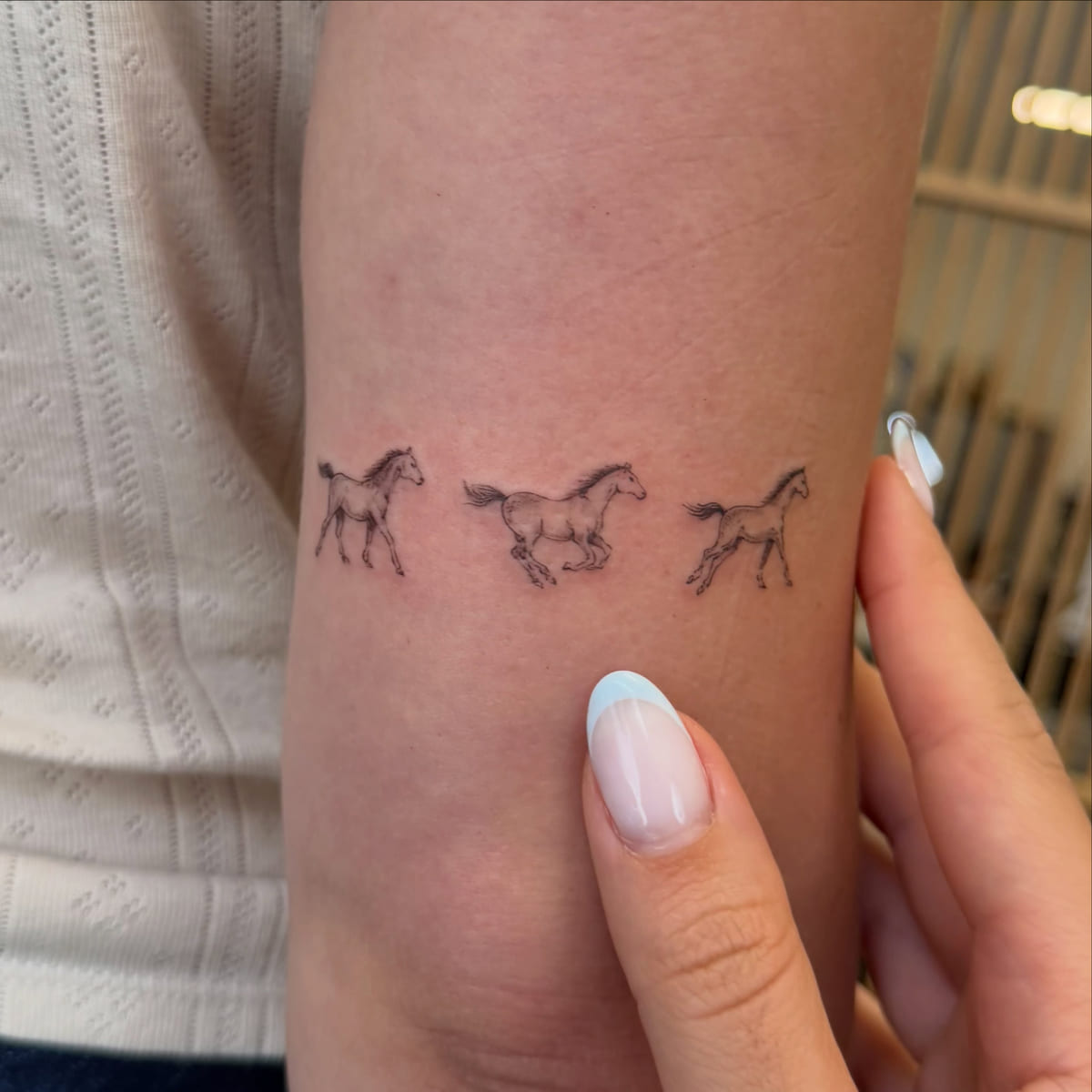 Three tiny running horses in a row, fine line tattoo