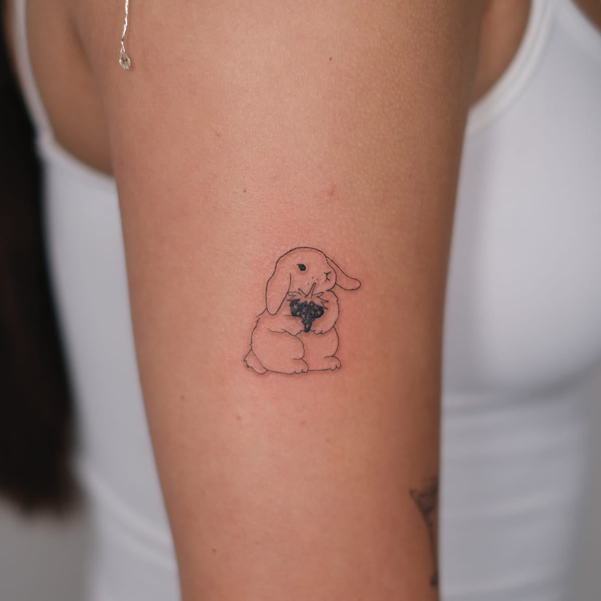 Lop eared rabbit holding berries, fine line tattoo