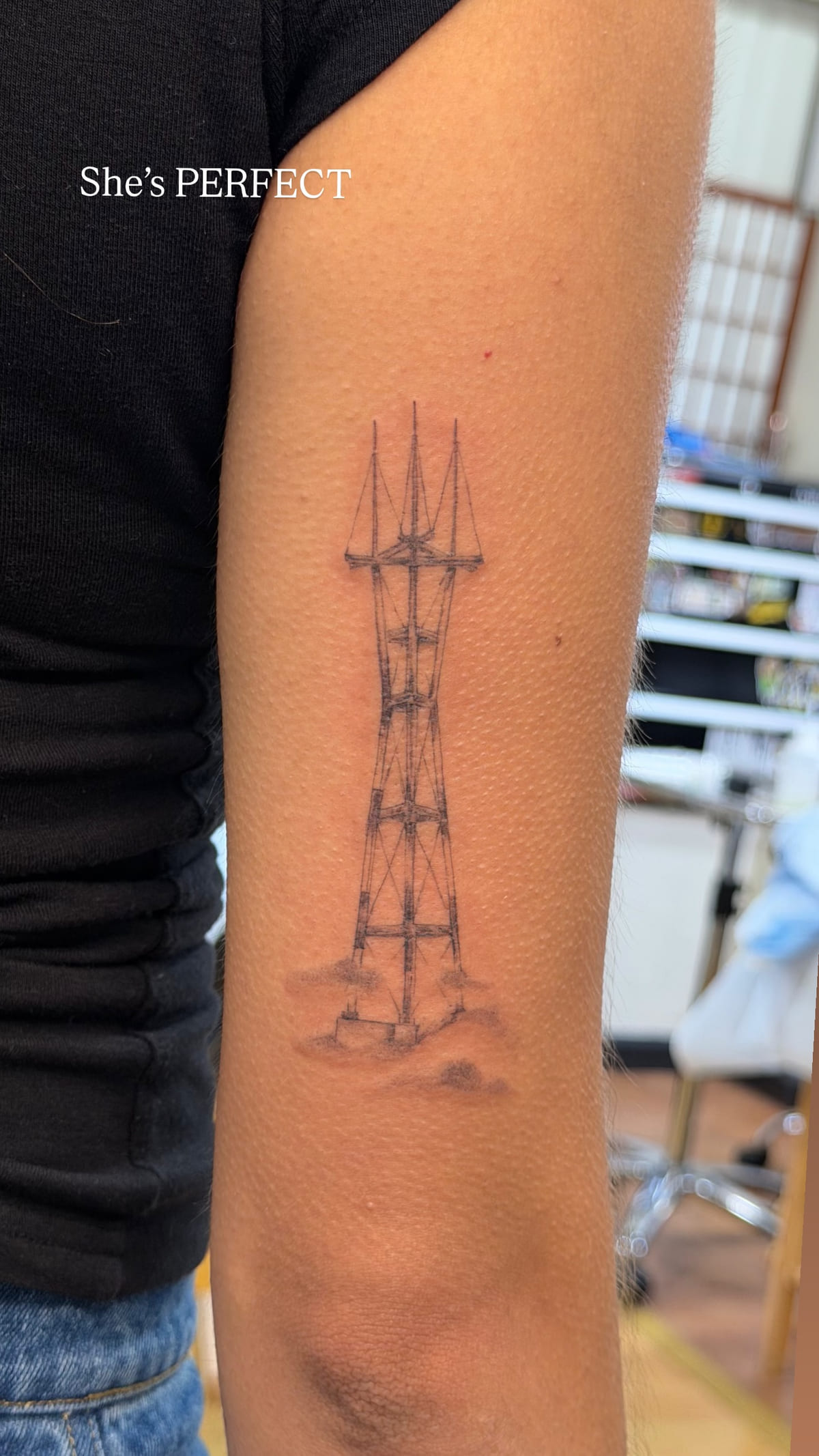 Sutro Tower rising from fog, back of an upper arm, fine line tattoo