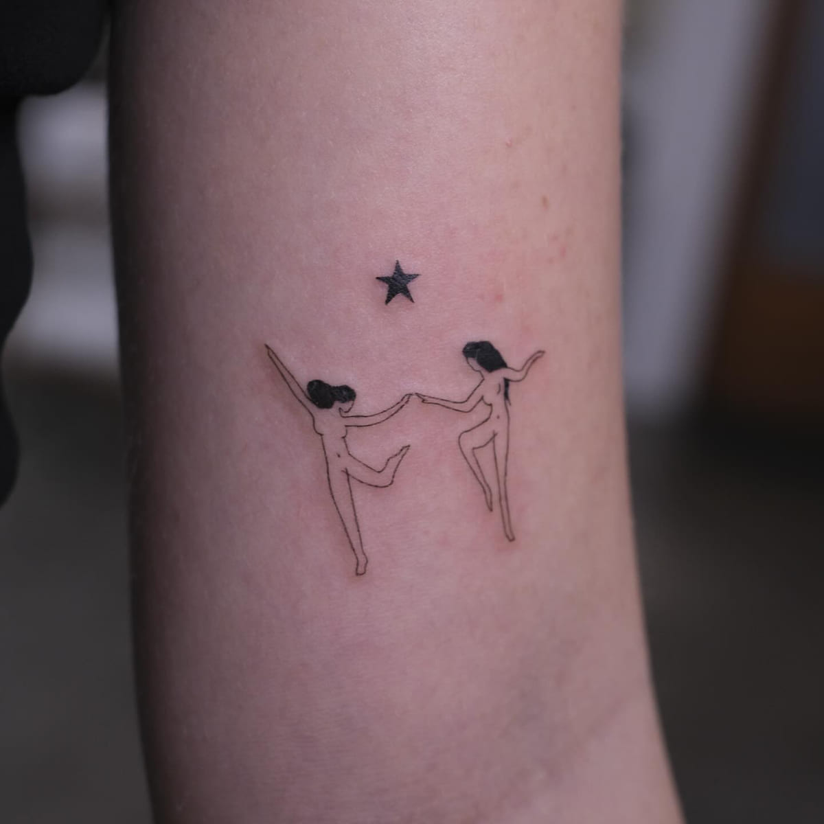 Two dancers holding hands under a star, fine line tattoo