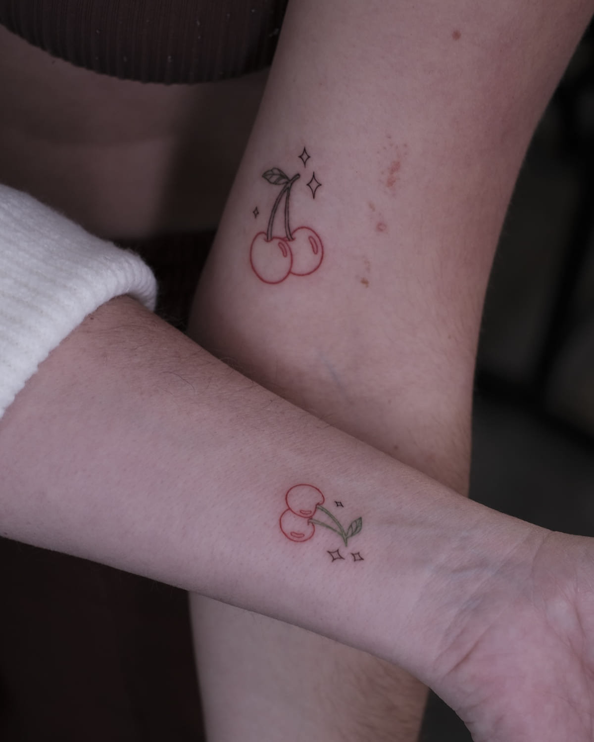 Two people with matching cherries, red fruit and green leaf, fine line tattoo