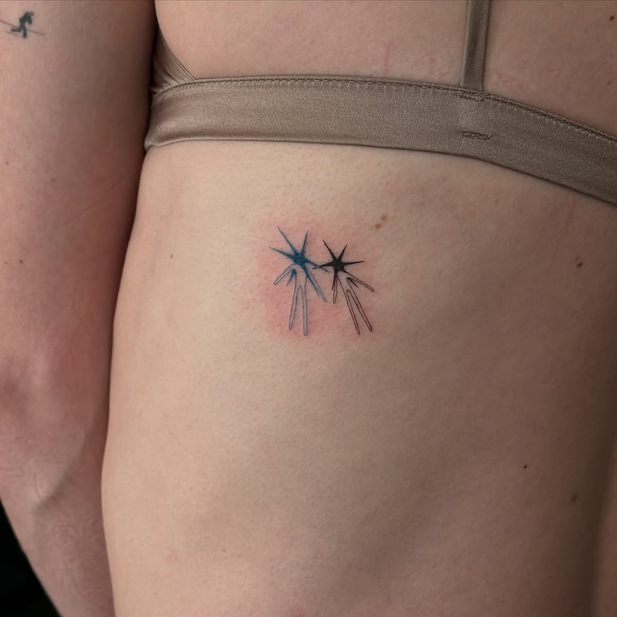Two falling stars, one blue and one black, fine line tattoo