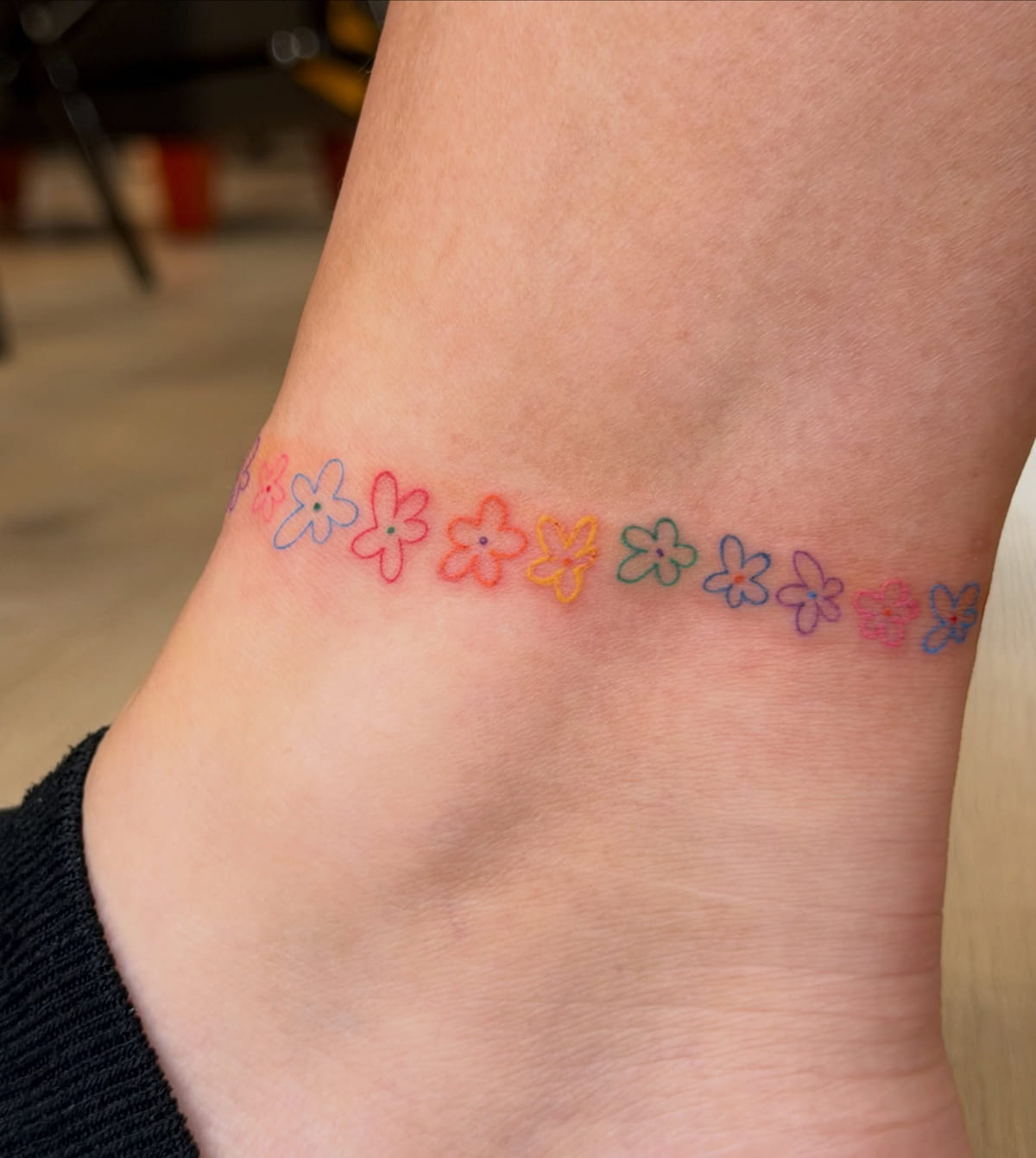 Anklet chain of tiny flowers in rainbow colors, fine line tattoo