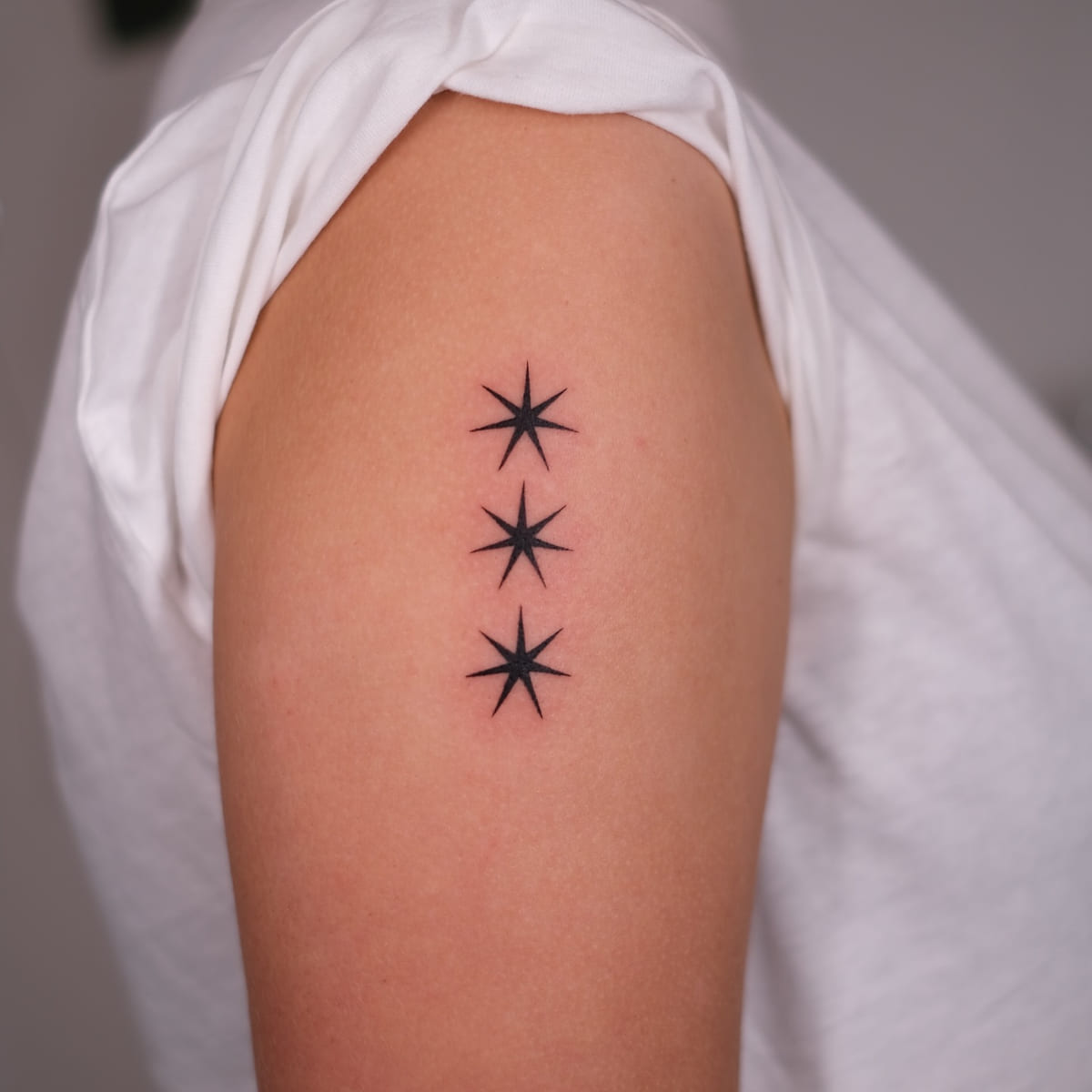 Three solid eight point stars in a column, fine line tattoo
